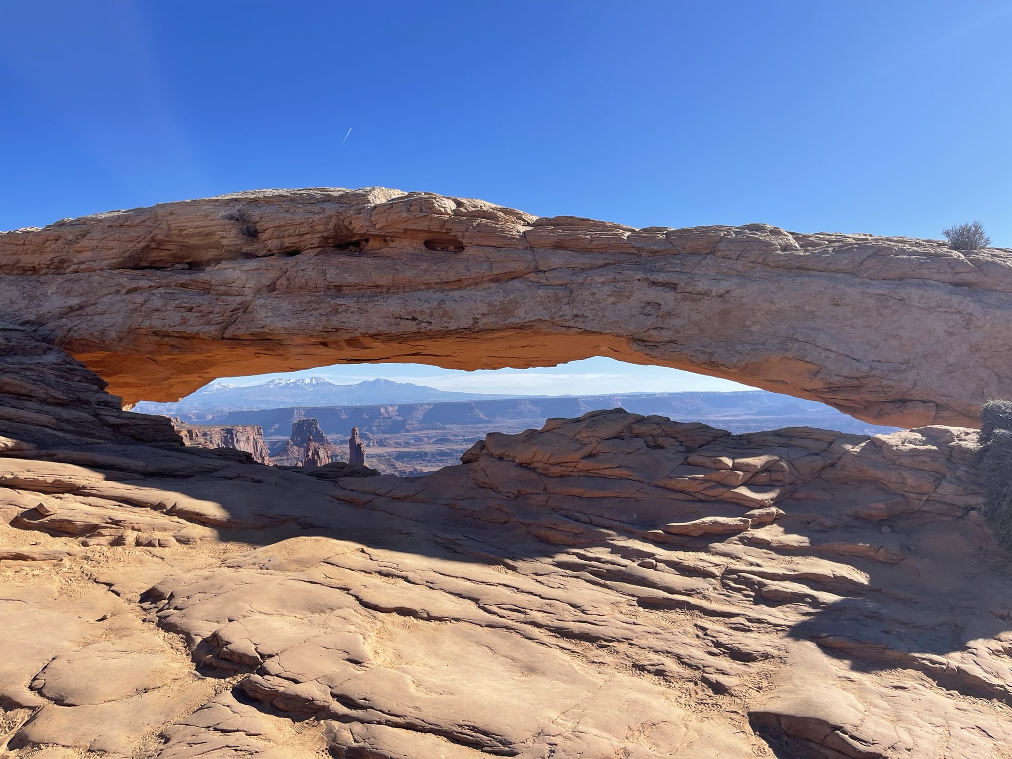 A sandstone arch framing distant mesas beneath a clear sky